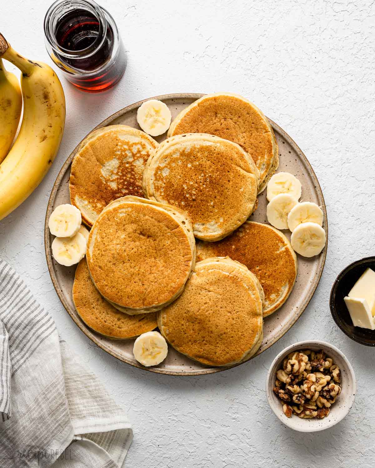 overhead view of a large plate filled with pancakes and sliced bananas surrounded with toppings.