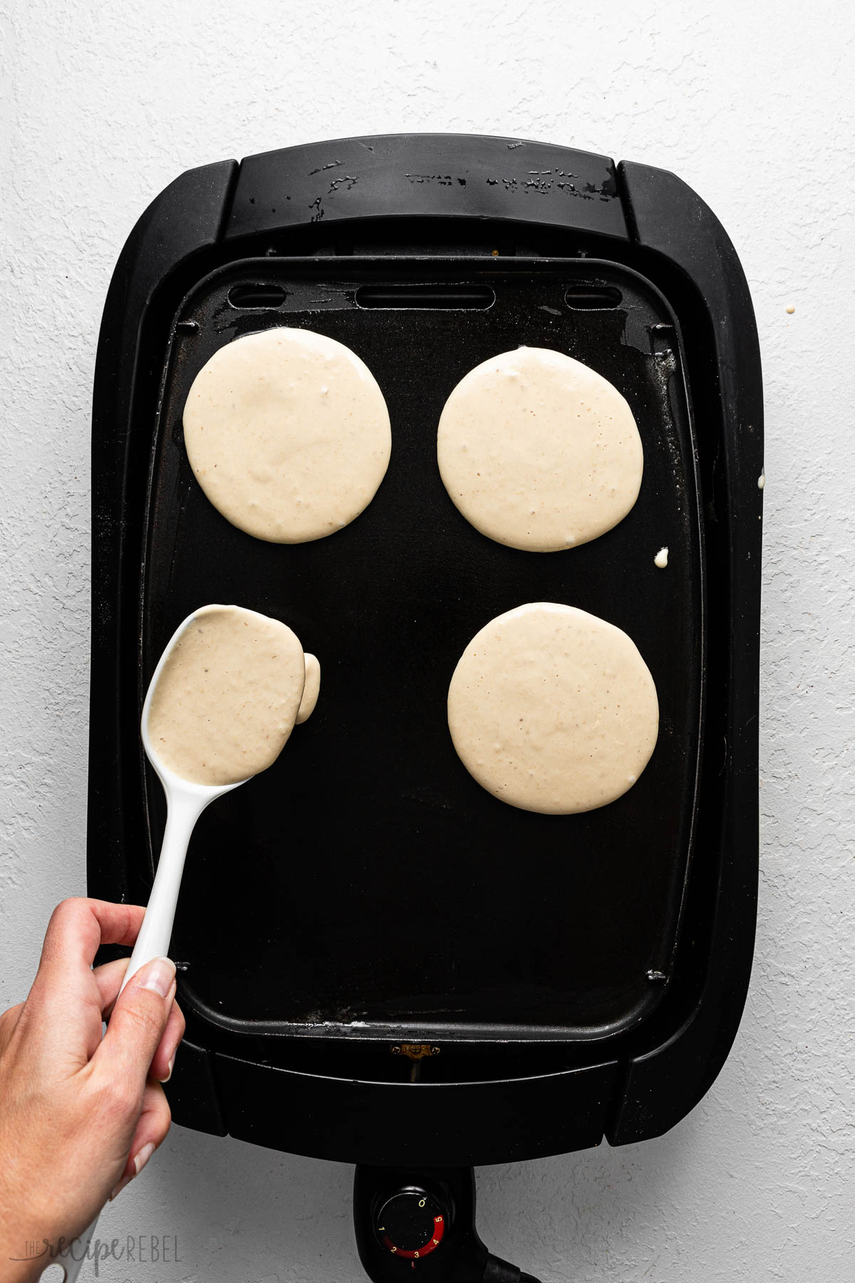 a black griddle with pancakes cooking and batter being poured on.