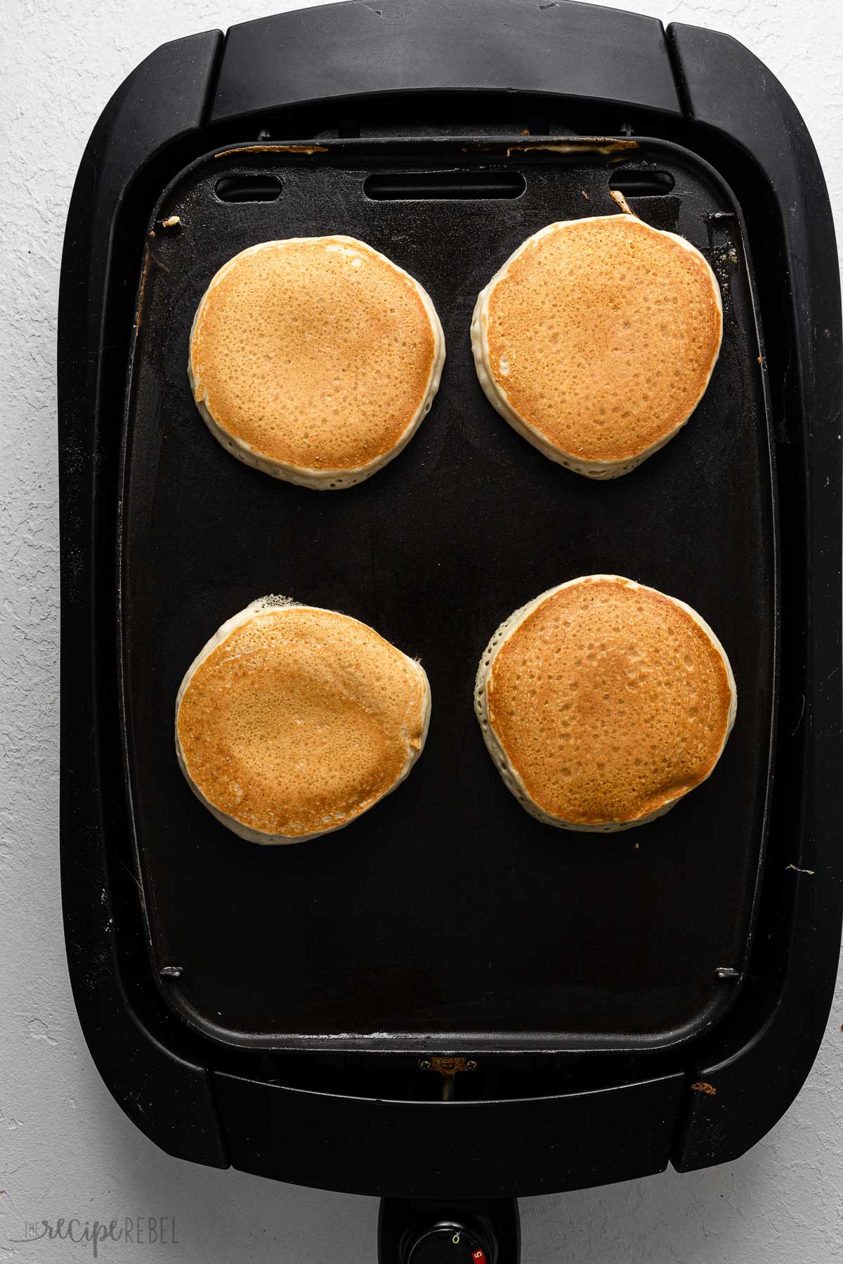 four golden banana pancakes on a black griddle.