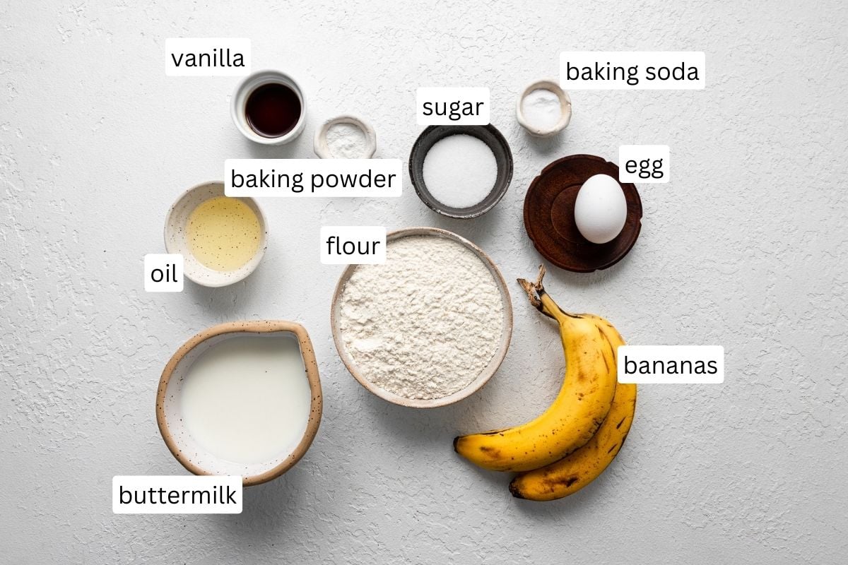 ingredients for banana pancakes in bowls on white surface.