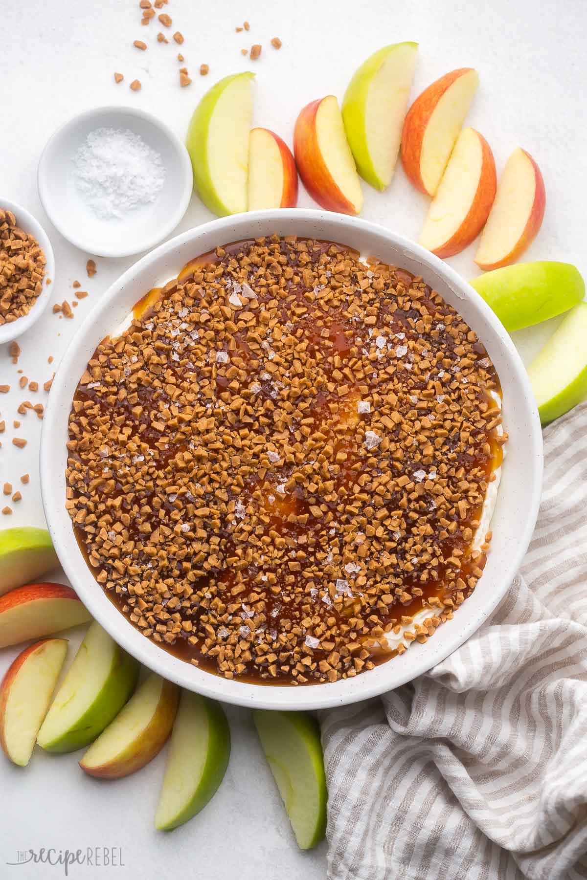 overhead view of a dish of caramel apple dip surrounded by sliced apples.