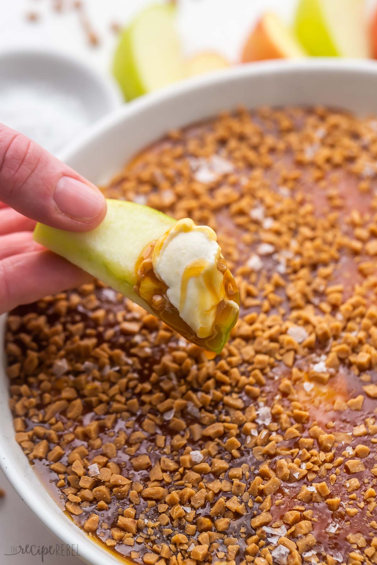 a hand holding an apple slice with caramel apple dip on it.