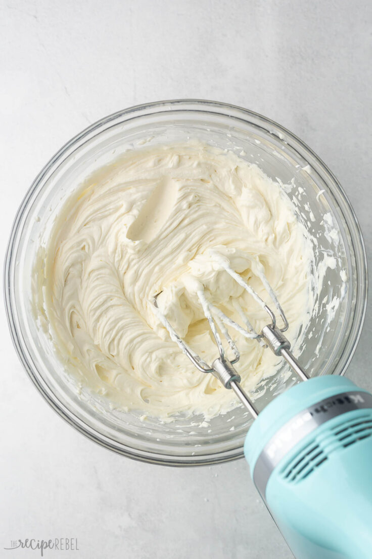 mixed cream cheese mixture in glass bowl with blue mixer beside.