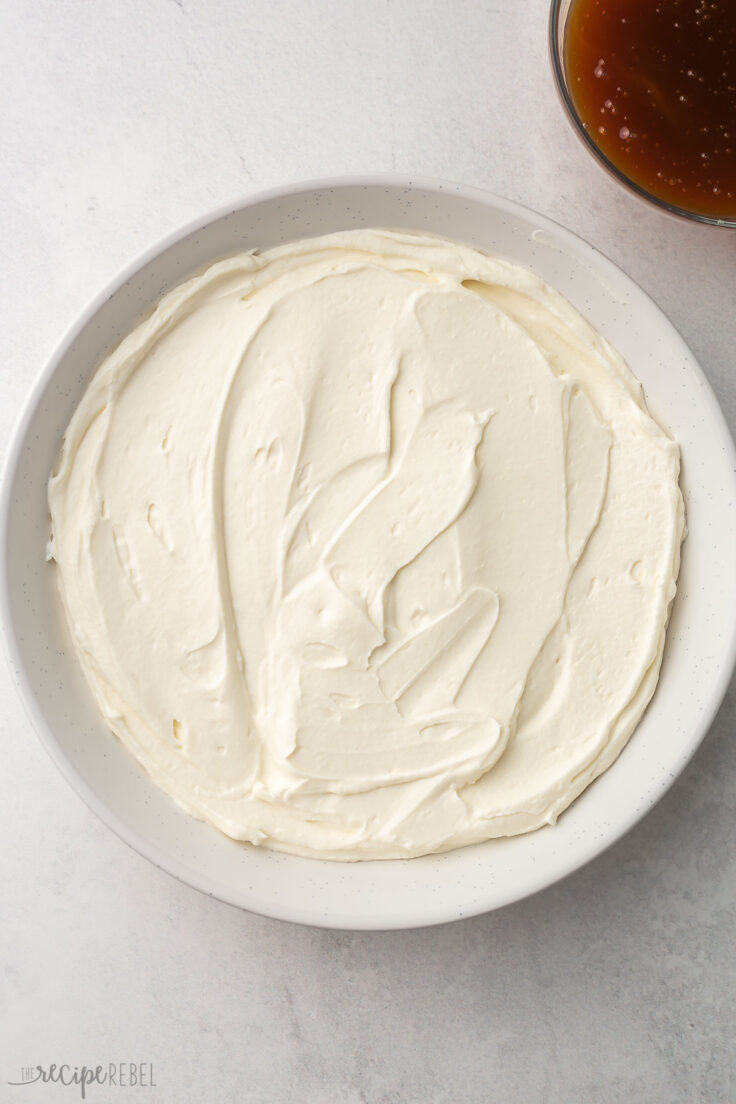 cream cheese mixture spread in white dish with bowl of caramel beside.