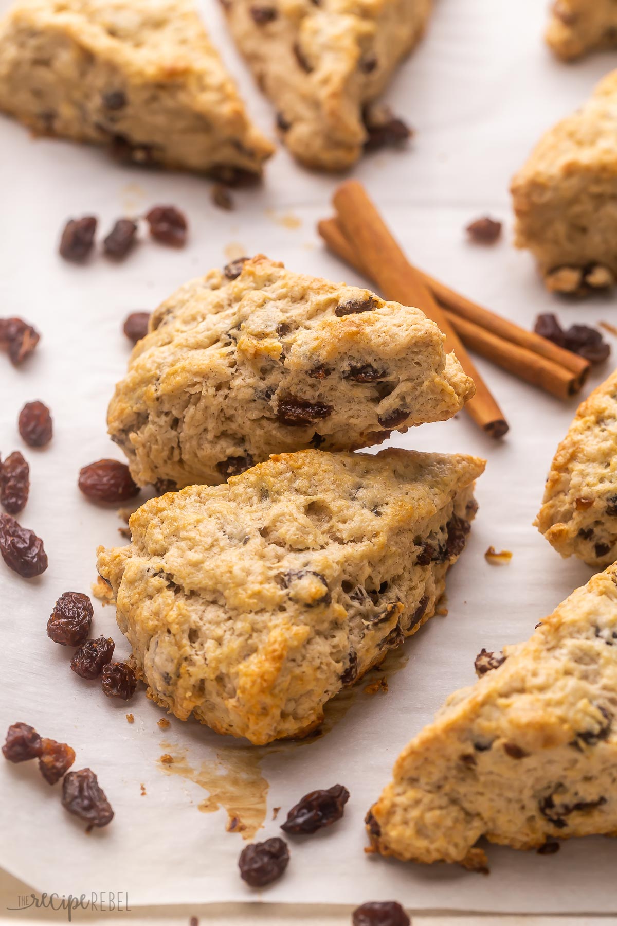 two cinnamon raisin scones on baking sheet with raisins around.
