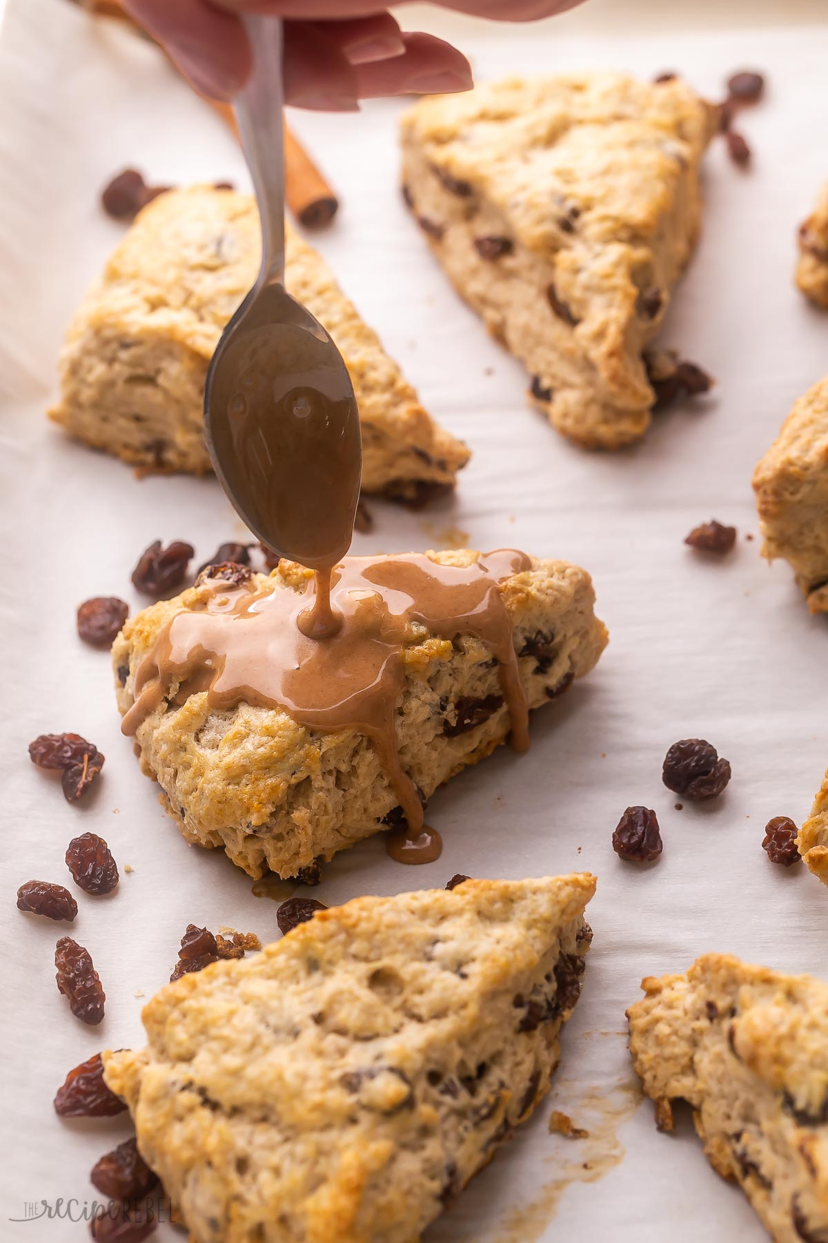 spoon drizzling cinnamon glaze on raisin scones.