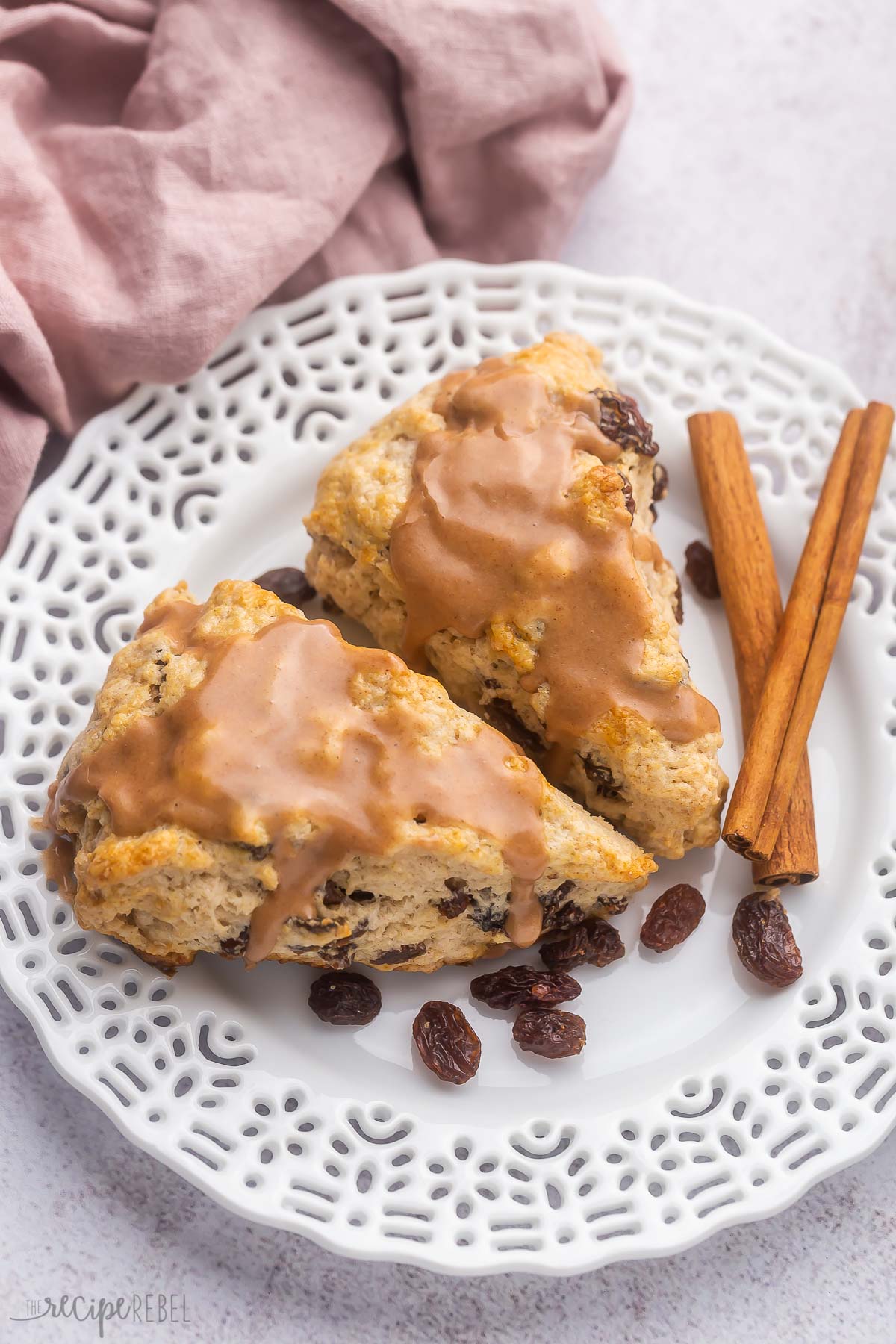 two glazed cinnamon scones on white plate with cinnamon sticks.