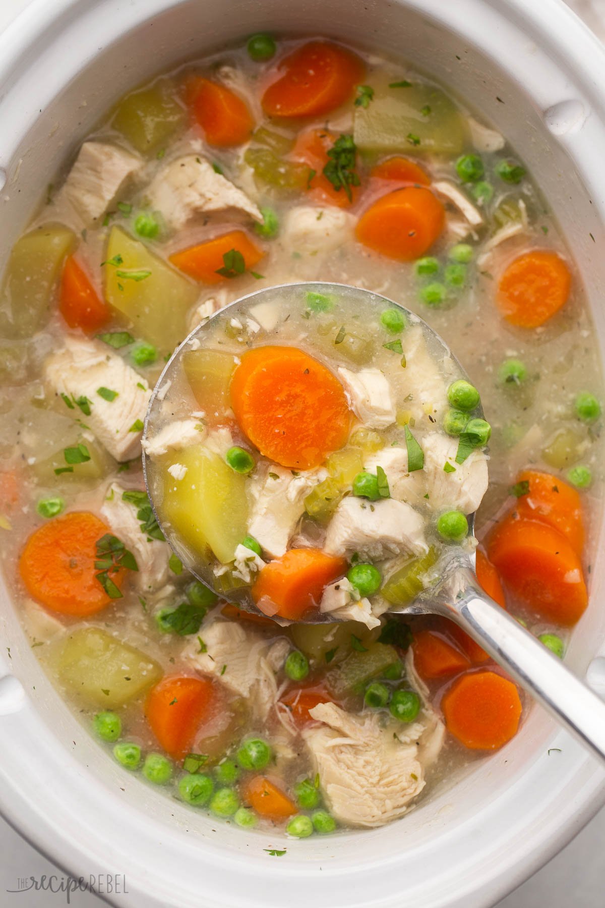 overhead shot of a crockpot full of chicken stew with steel ladle in.