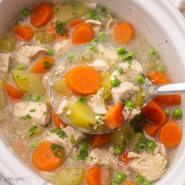 close up view of a ladle full of crockpot chicken stew above crockpot.