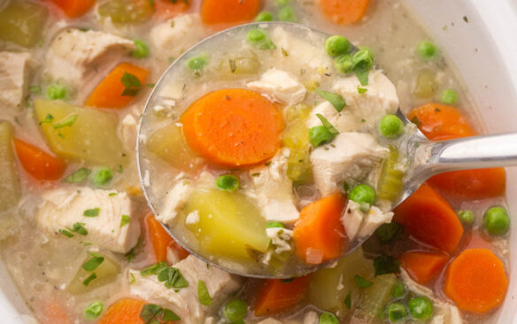 close up view of a ladle full of crockpot chicken stew above crockpot.