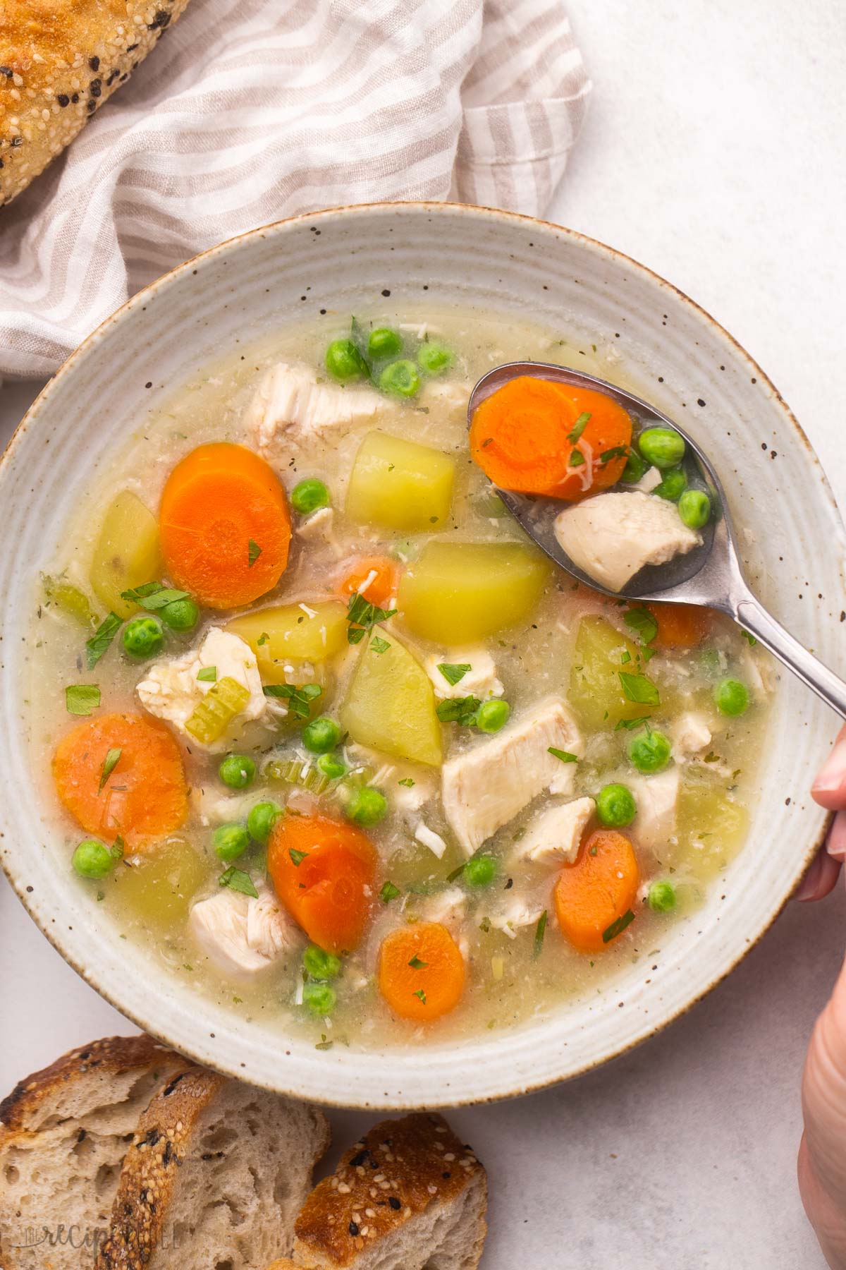 overhead shot of a full bowl of crockpot chicken stew with a spoon scooping some out.