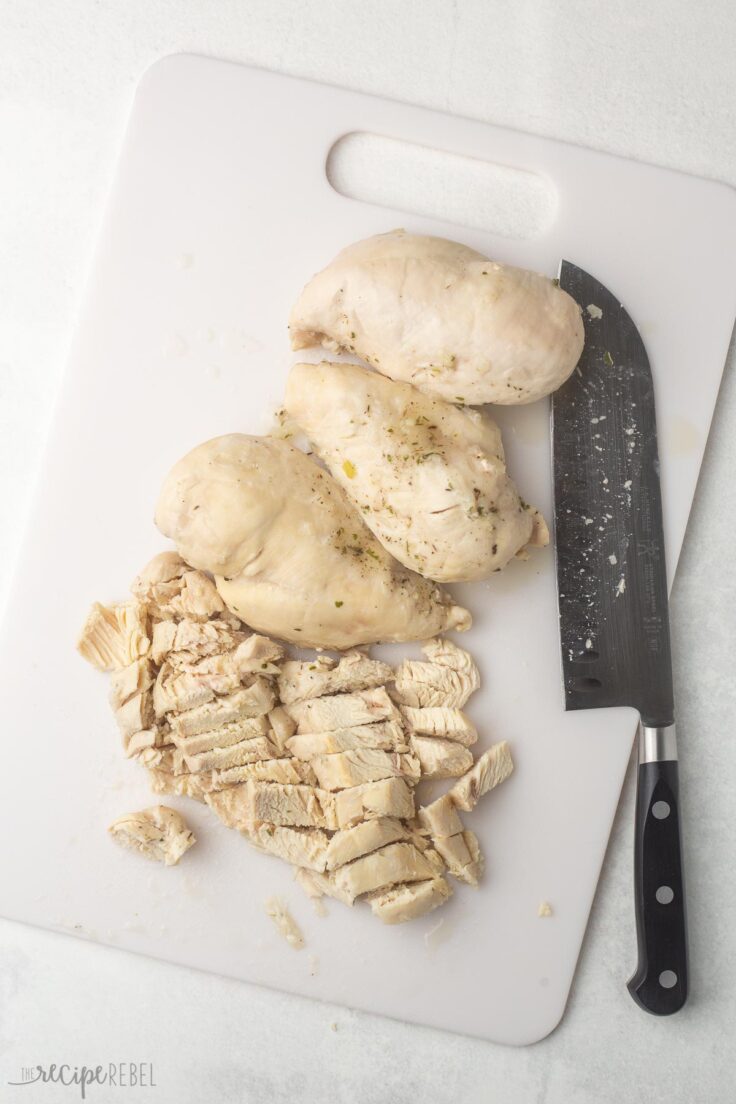 chicken breasts and knife lying on a white cutting board.
