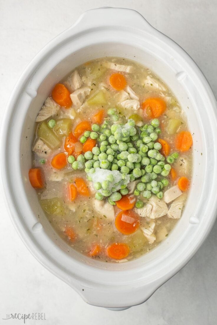 white crockpot with chopped chicken and frozen peas added in.