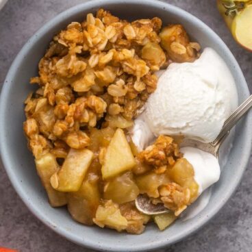 a spoon scooping ice cream and apple crisp out of a blue bowl.