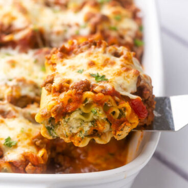 a steel spatula scooping a piece of lasagna roll up out of a white baking dish.