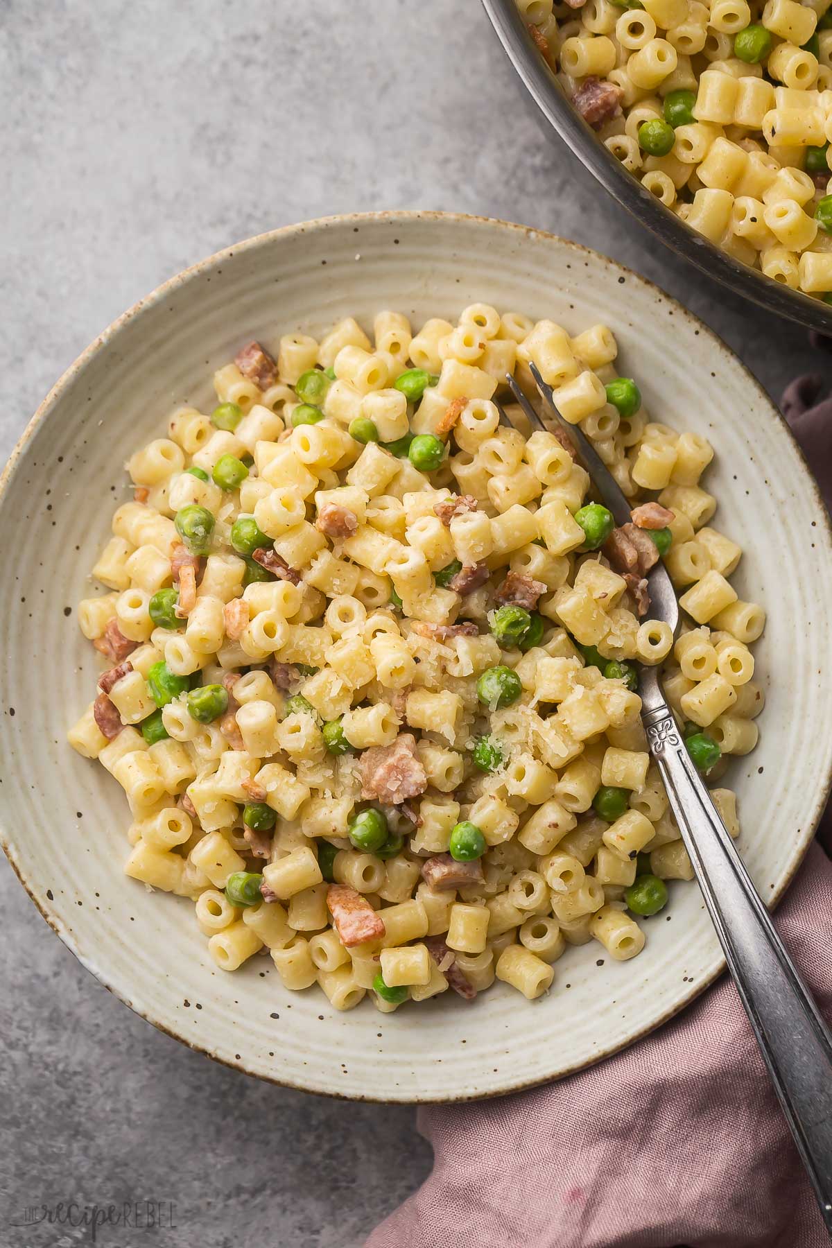 plate filled with ditalini bacon and pea pasta with steel fork in it.