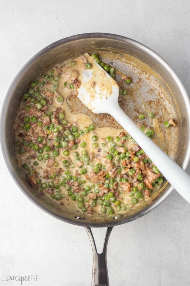 overhead of pan with bacon, peas and sauce on grey surface.