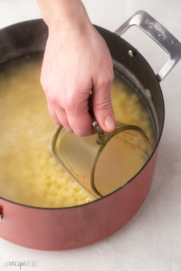 glass measuring cup scooping pasta water out of red pot.