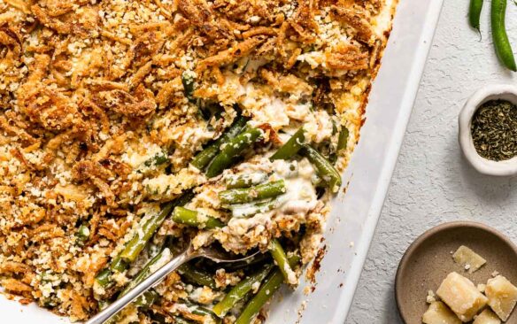 close up a spoon scooping green bean casserole out of white baking dish.