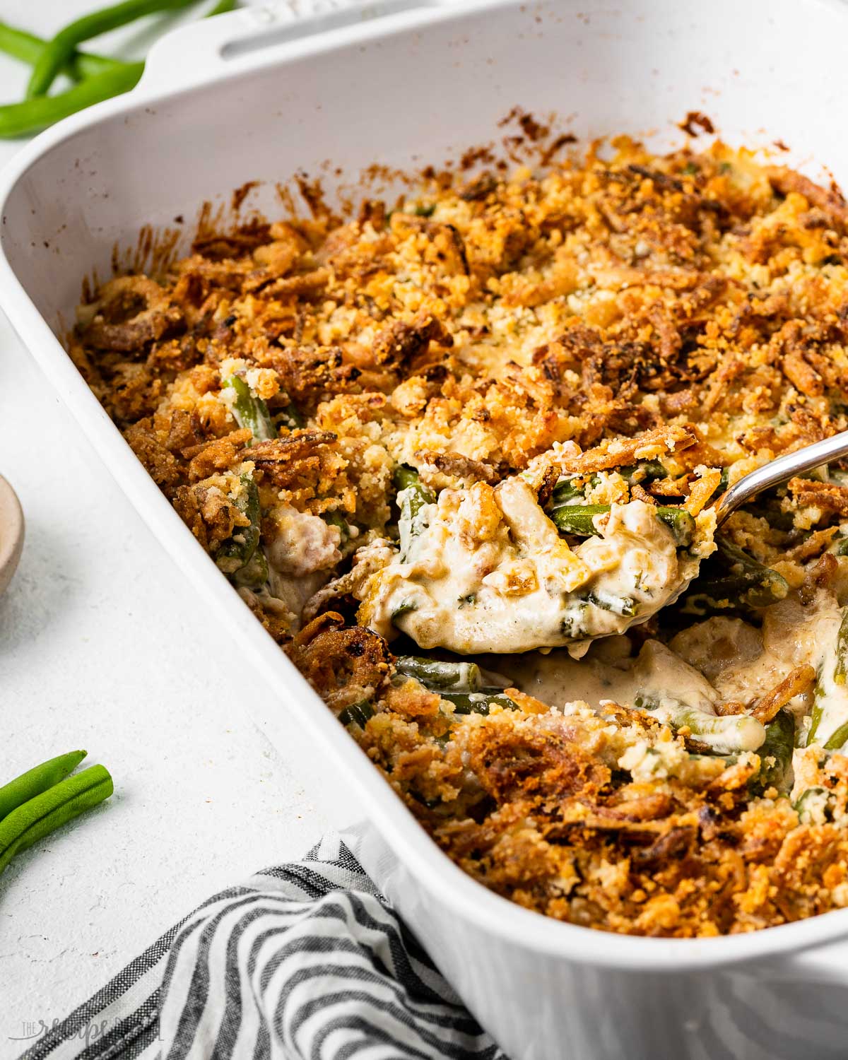 green bean casserole being spooned out of a white baking dish.