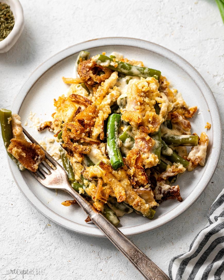 a forkful of green bean casserole lying beside a white plate full.