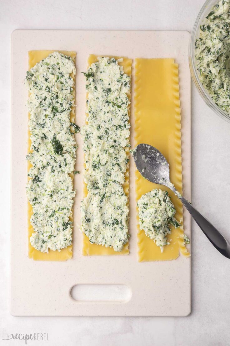 lasagna noodles being topped with filling on a white cutting board.