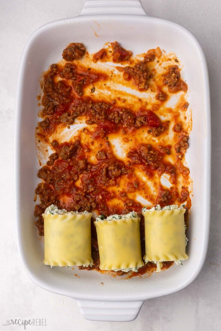 white baking dish partially filled with lasagna rolls and sauce.