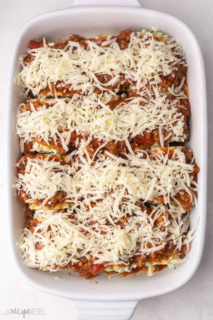 overhead shot of white baking dish filled with lasagna roll ups topped with shredded cheese.