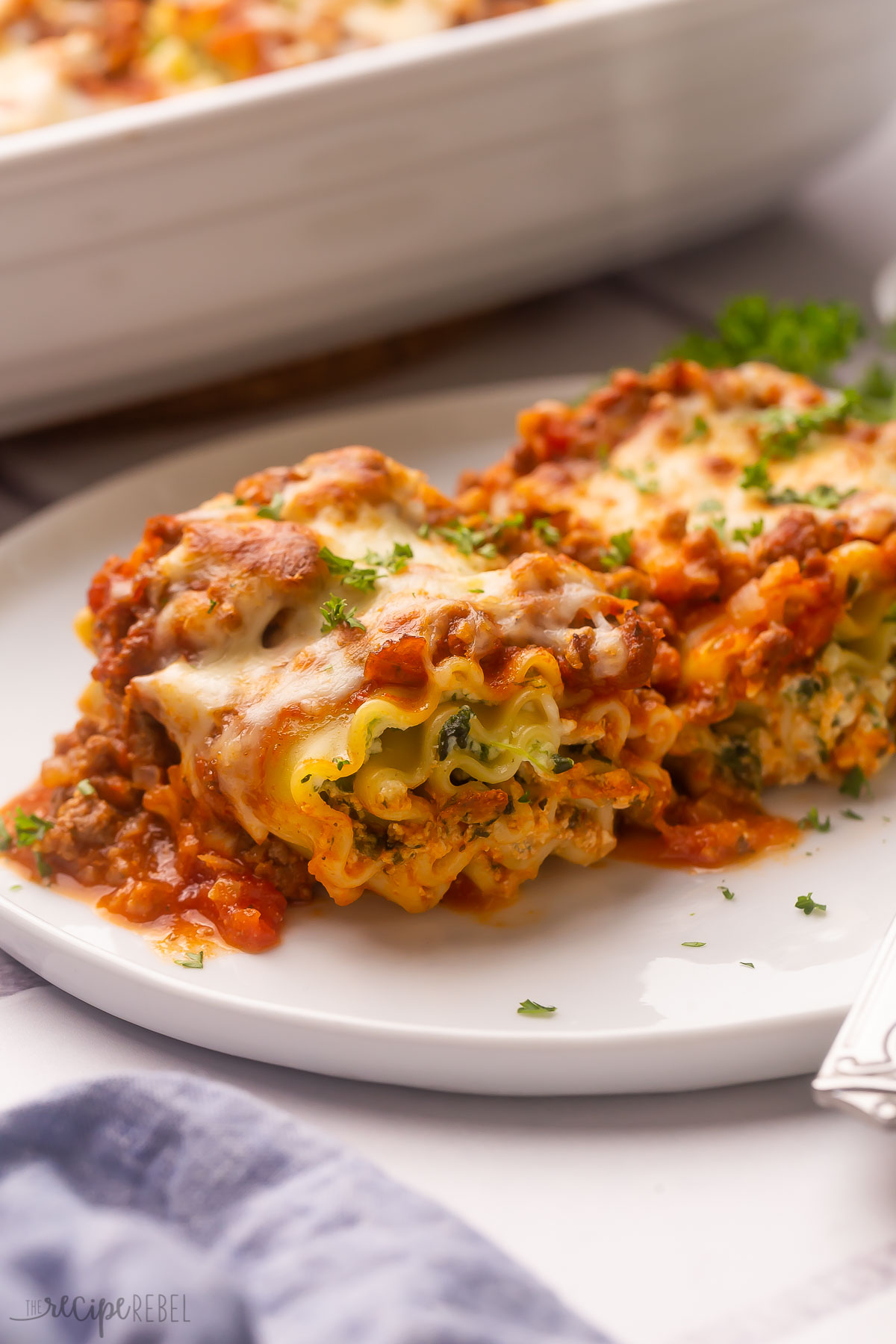 two pieces of lasagna roll ups on a white plate garnished with parsley.