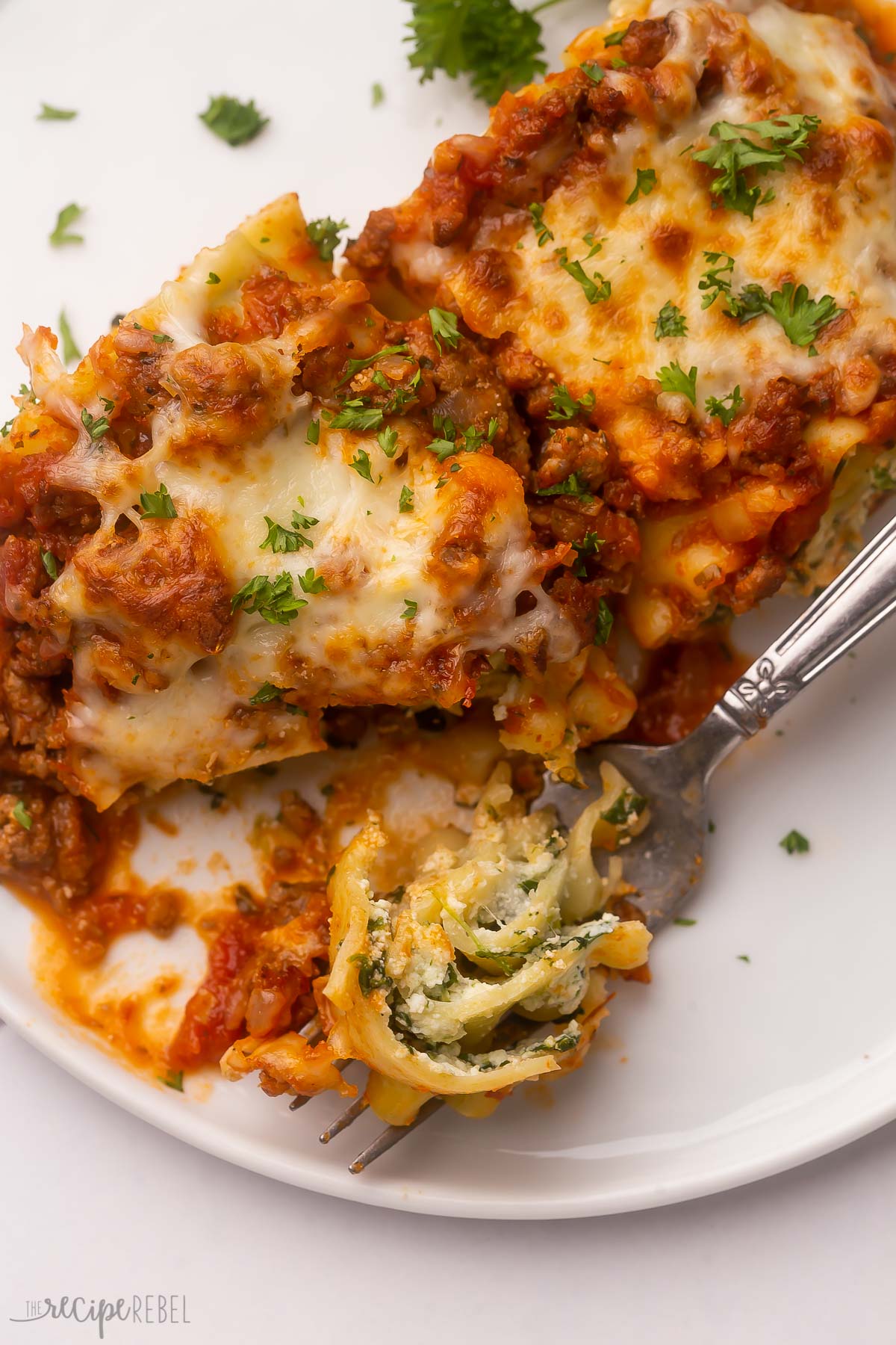 close up of a fork full of lasagna roll ups on a white plate.