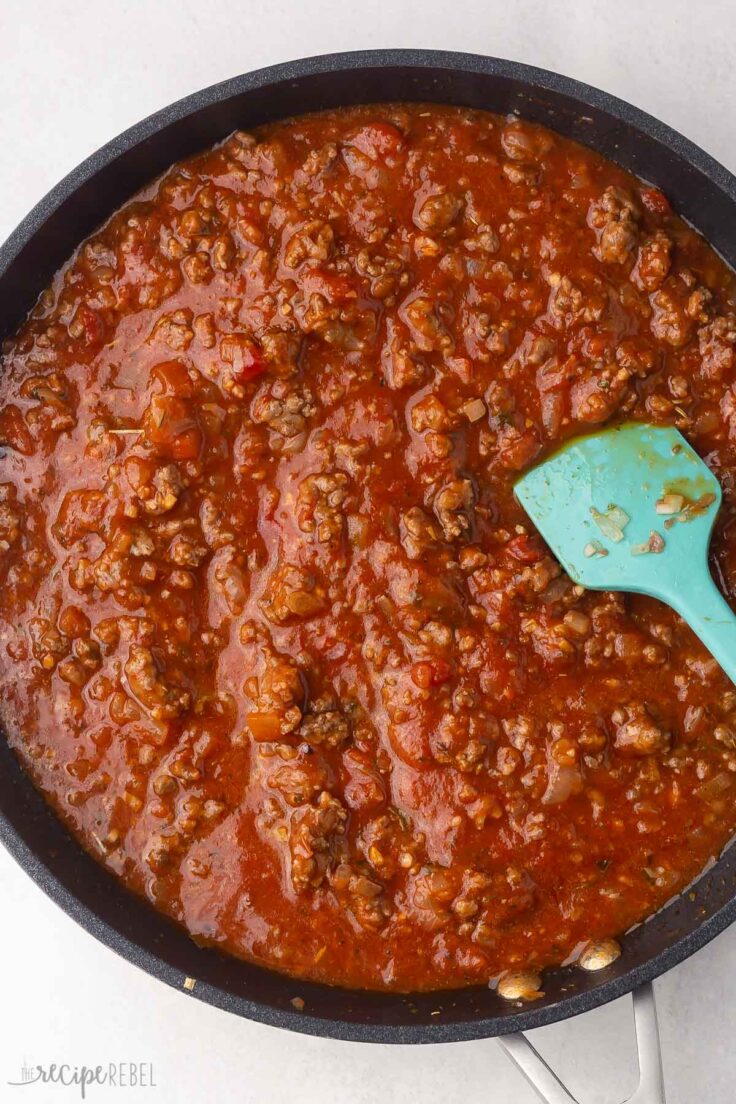 black frying pan with sauce, meat and blue spatula in it.