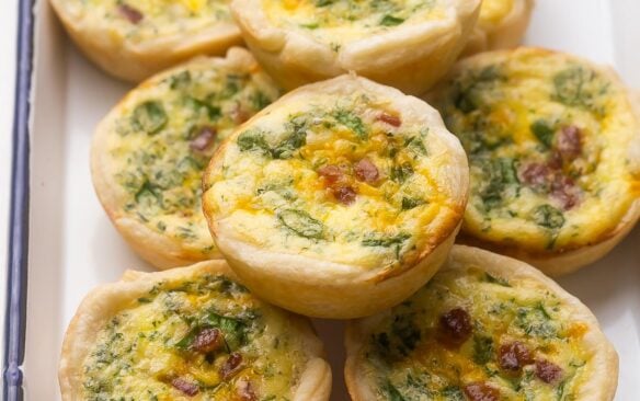 close up of stacked mini quiche in white dish.