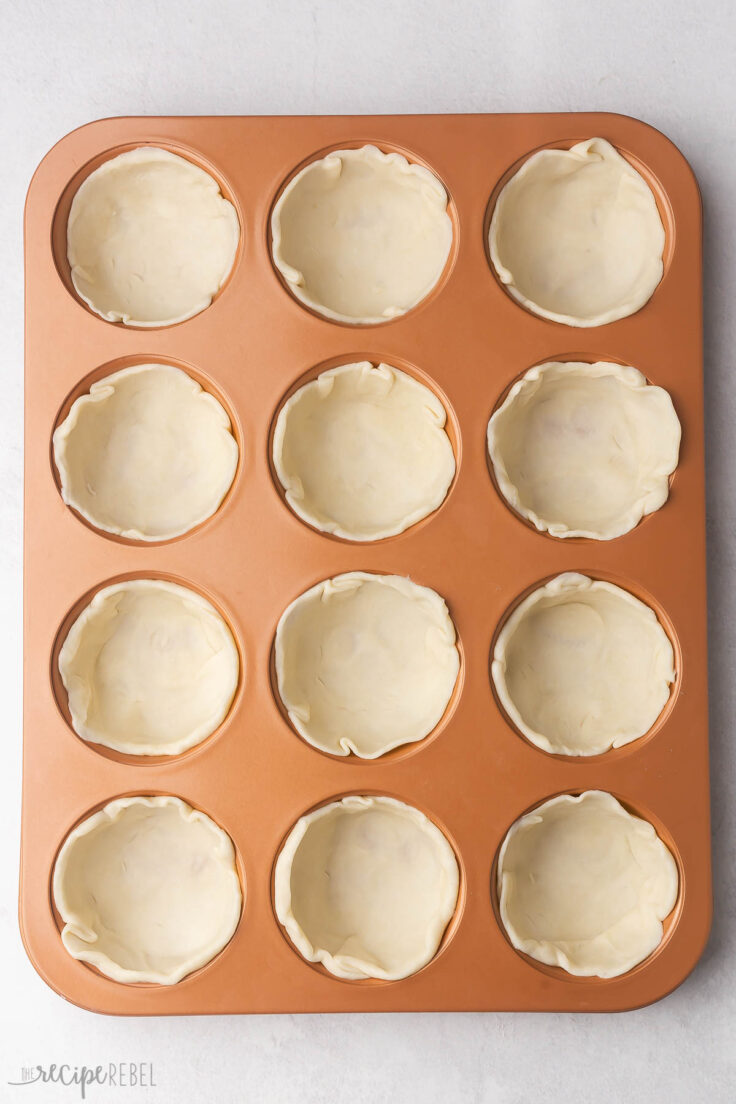 cooper coloured muffin pan with dough pressed in.