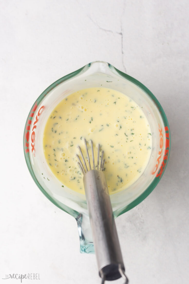 whisk and eggs in a glass measuring cup on a grey surface.