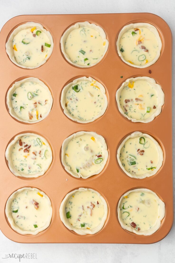 muffin pan with mini quiche shells filled and ready to be baked.