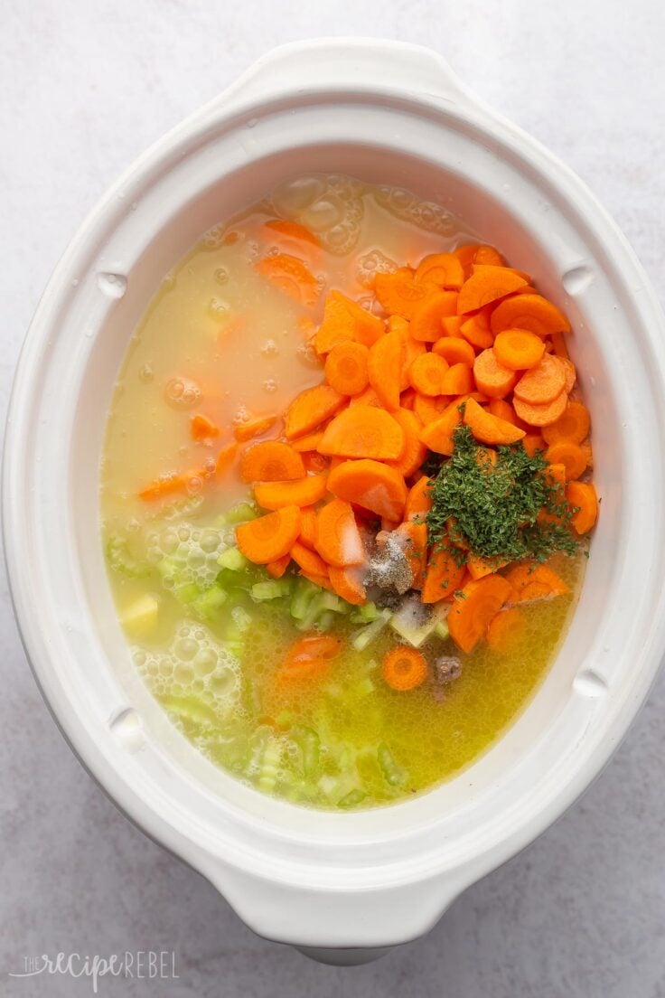 white slow cooker filled with broth, vegetables and spices.