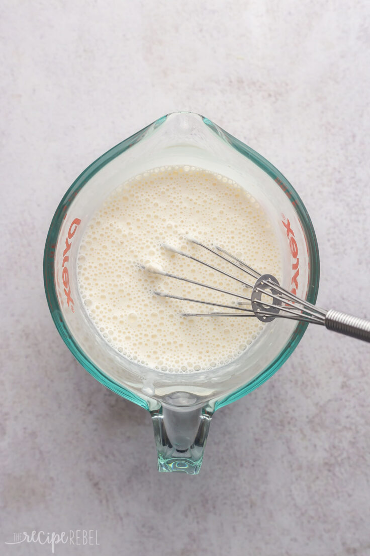 glass measuring cup with mixed cream, corn starch and steel whisk.