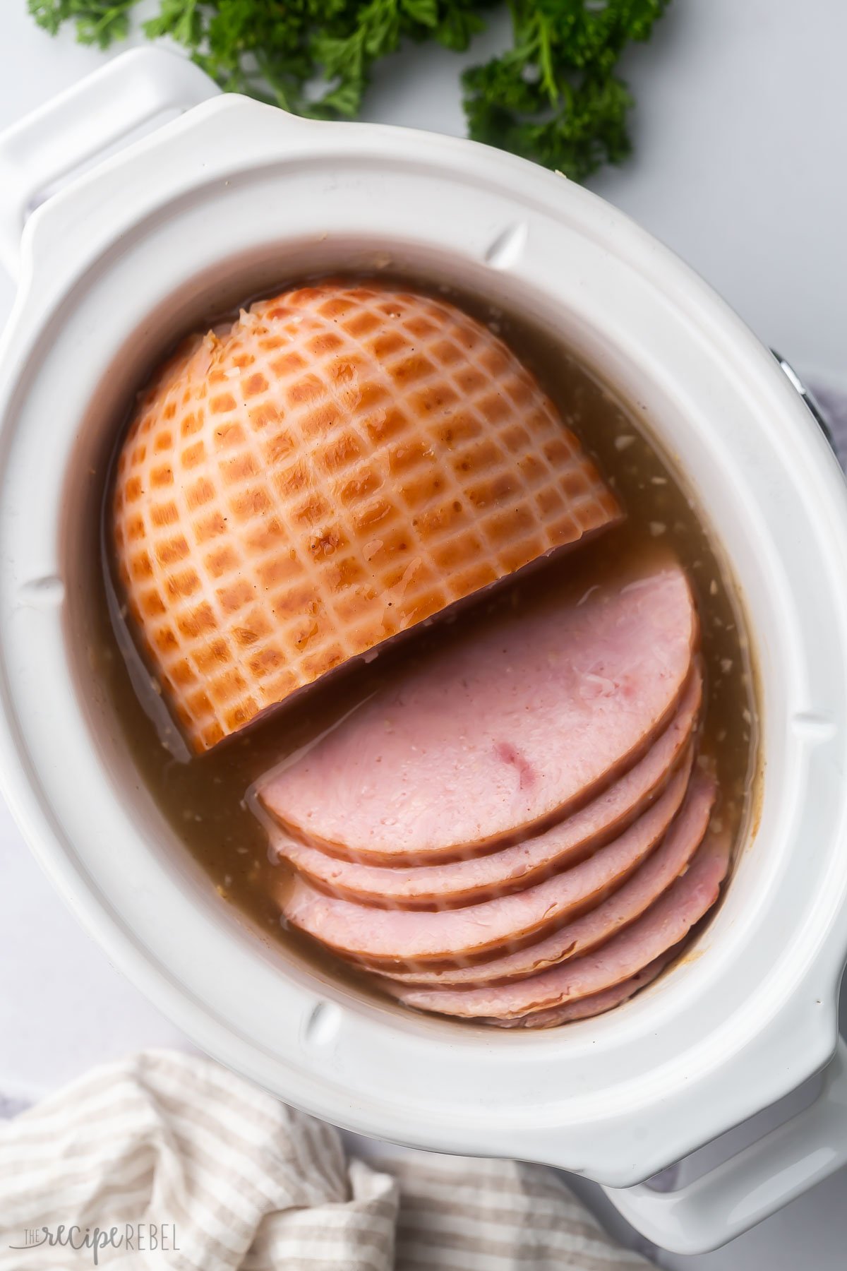 overhead view of a white slow cooker filled with sliced honey glazed ham.