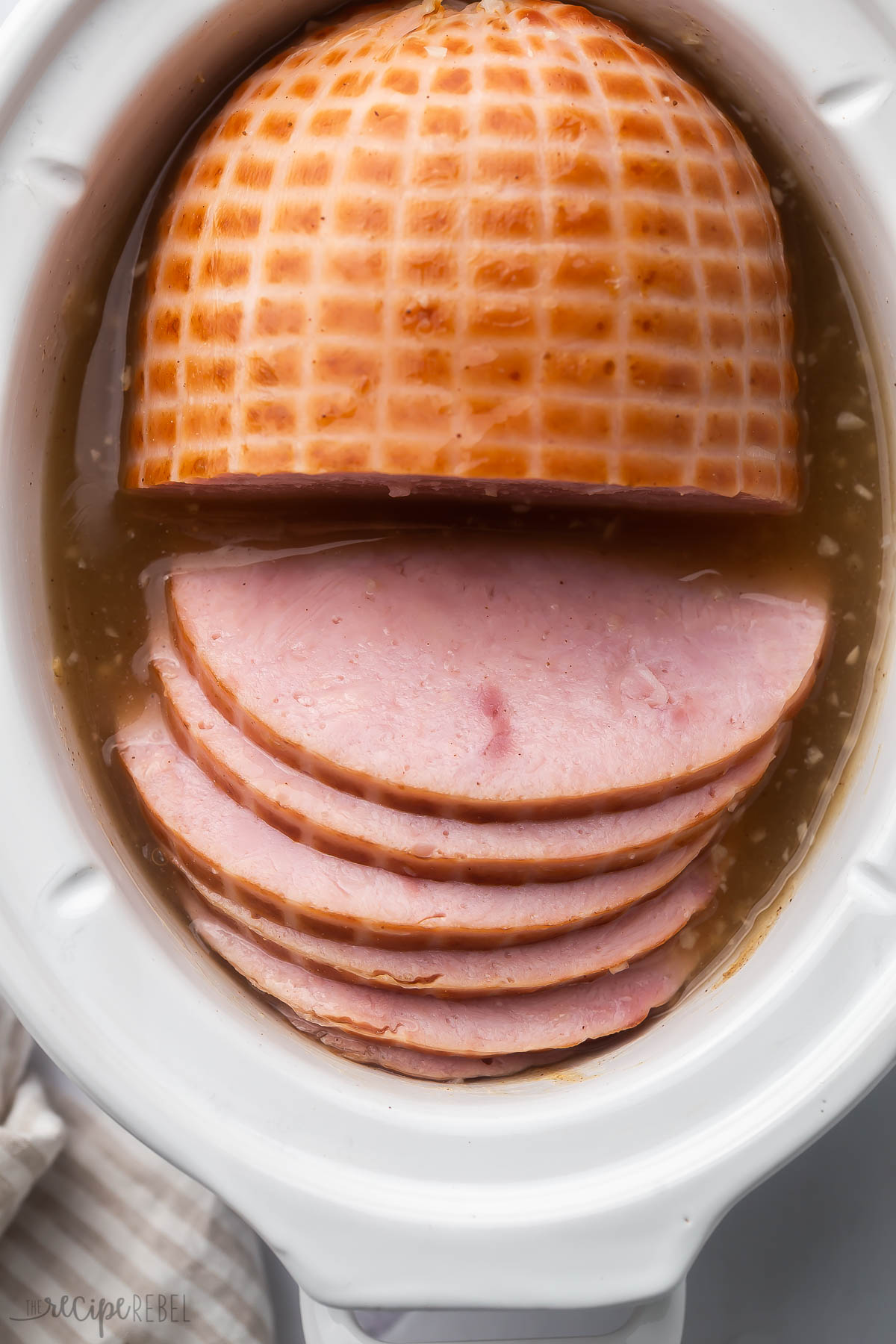 cooked ham in white slow cooker partially sliced.