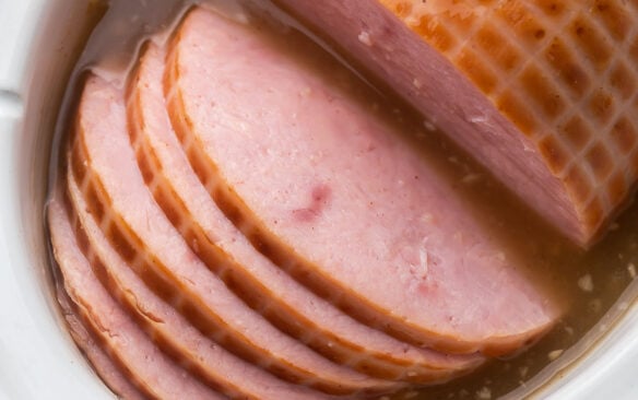 close up of ham slices in white slow cooker.