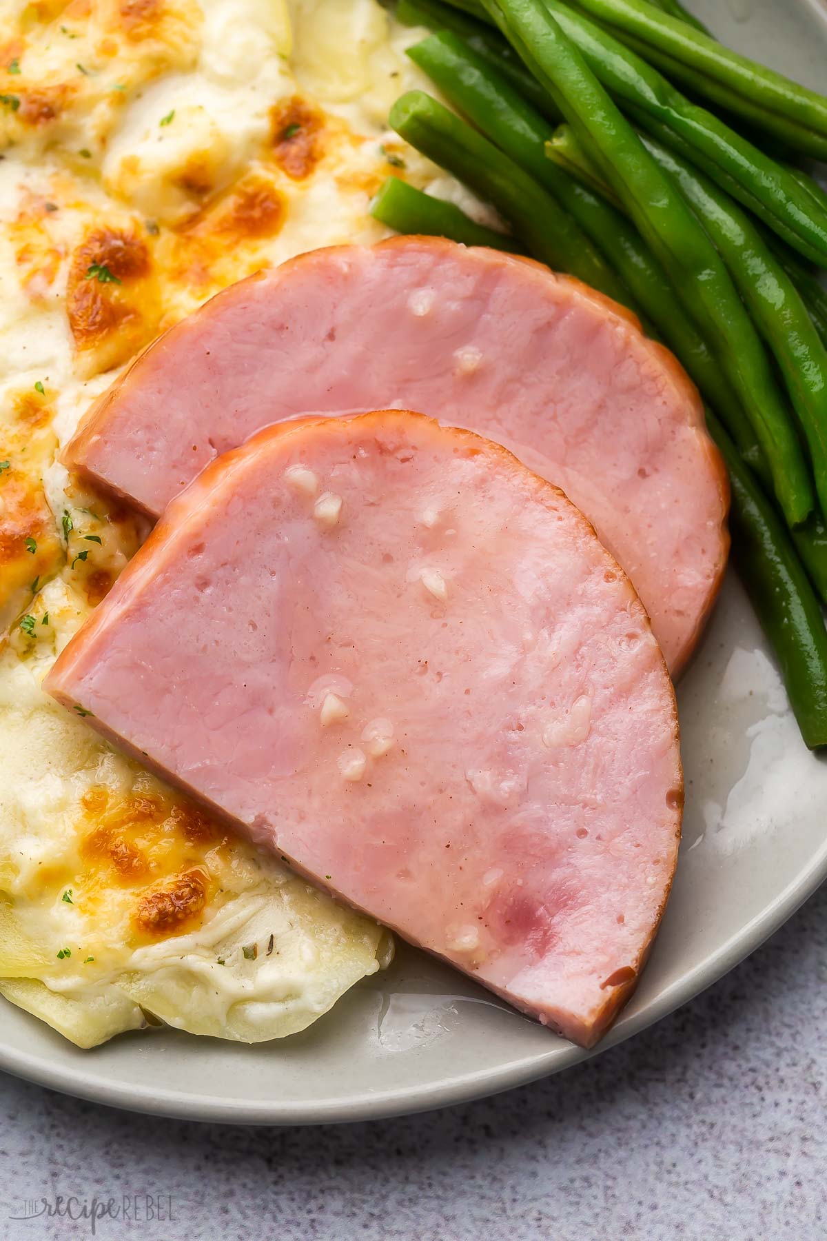 two slices of honey glazed ham on a plate with potatoes and green beans.