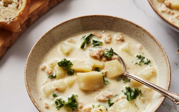 a filled bowl of zuppa toscana soup with sliced bread beside.