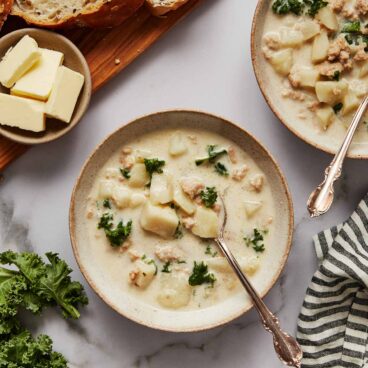 overhead shot of bowls of slow cooker zuppa toscana with bread and butter beside.