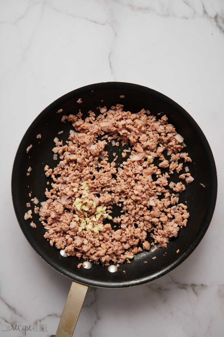 overhead view of cooked sausage and onions in a black frying pan.