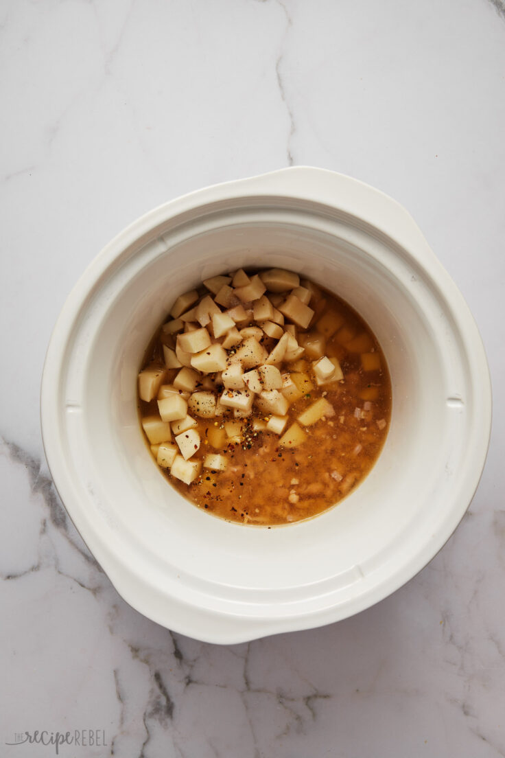 white slow cooker with potatoes, spices, and liquid in.