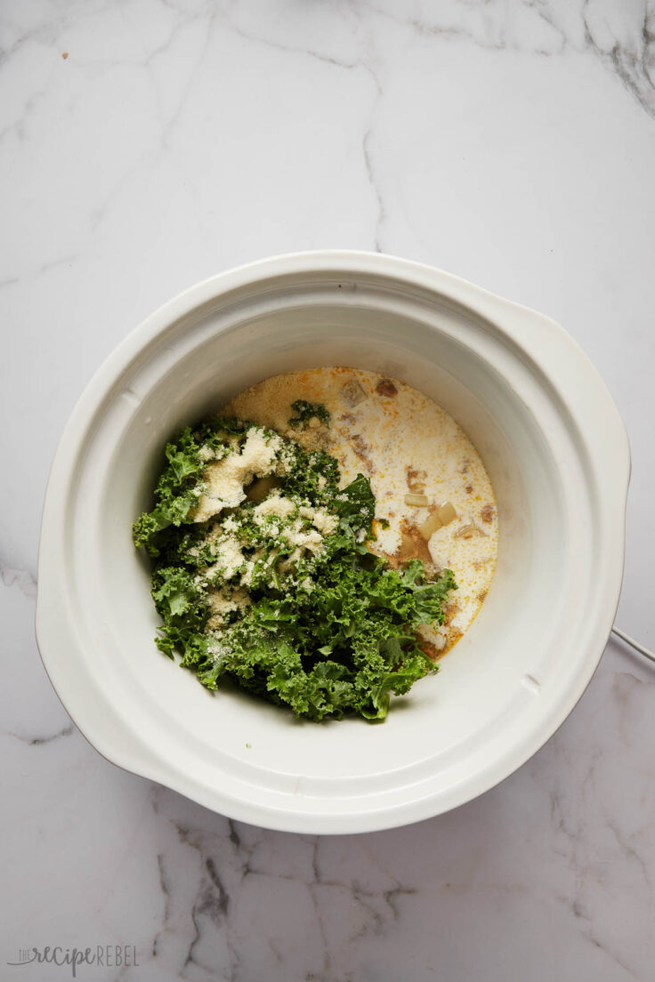 overhead view of white slow cooker with kale and other ingredients added.