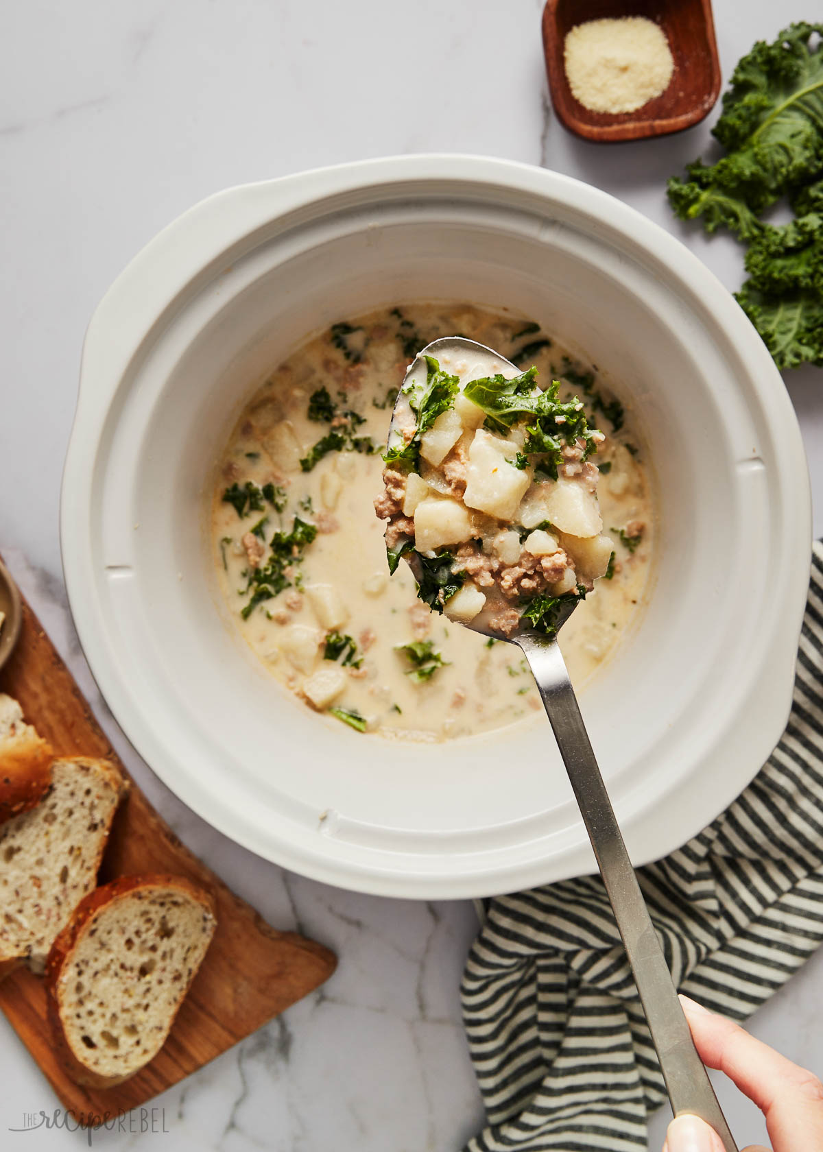 This easy Slow Cooker Zuppa Toscana is a creamy Tuscan soup full of Italian sausage, kale, potatoes, and Parmesan. It's hearty, creamy, and perfect for the colder months! There's a step-by-step recipe video down in the recipe card, too! #soup #slowcooker #crockpot | soup recipes | dinner ideas | easy dinner recipes | crockpot recipes | slow cooker meals Top view of a metal ladle scooping slow cooker zuppa toscana soup out of slow cooker.