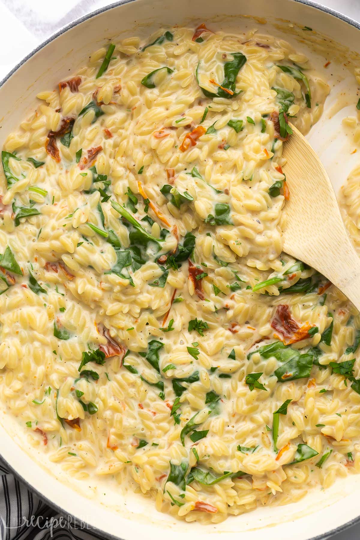 sun dried tomato spinach orzo in white dish with wooden ladle.