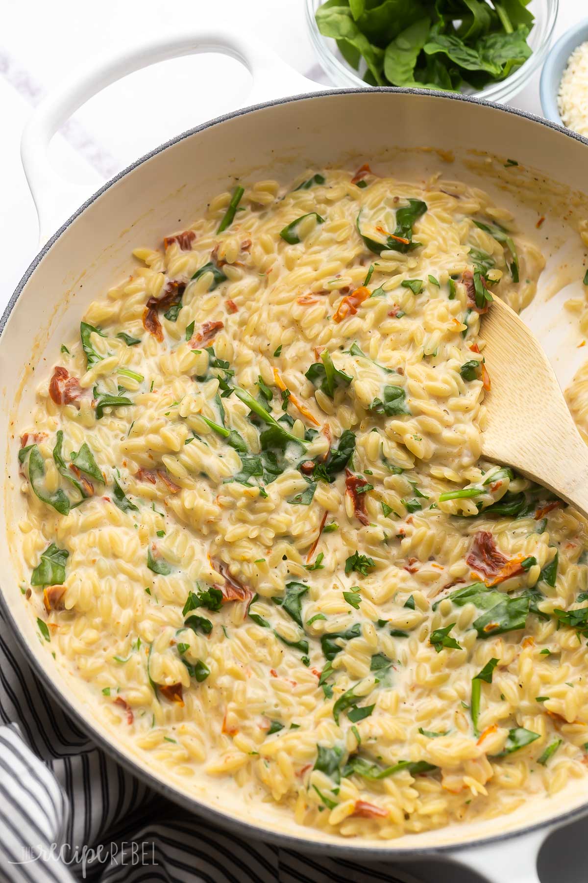wooden ladle scooping sun dried tomato spinach orzo out of white dish.