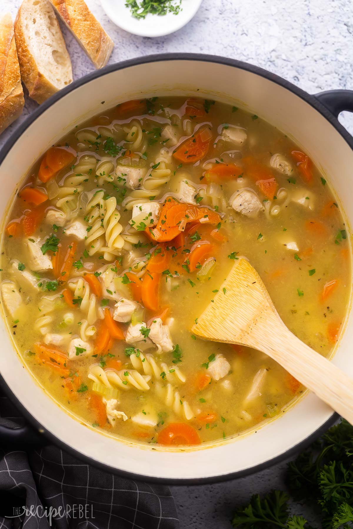 overhead view of cooked turkey noodle soup in pot with bread beside.